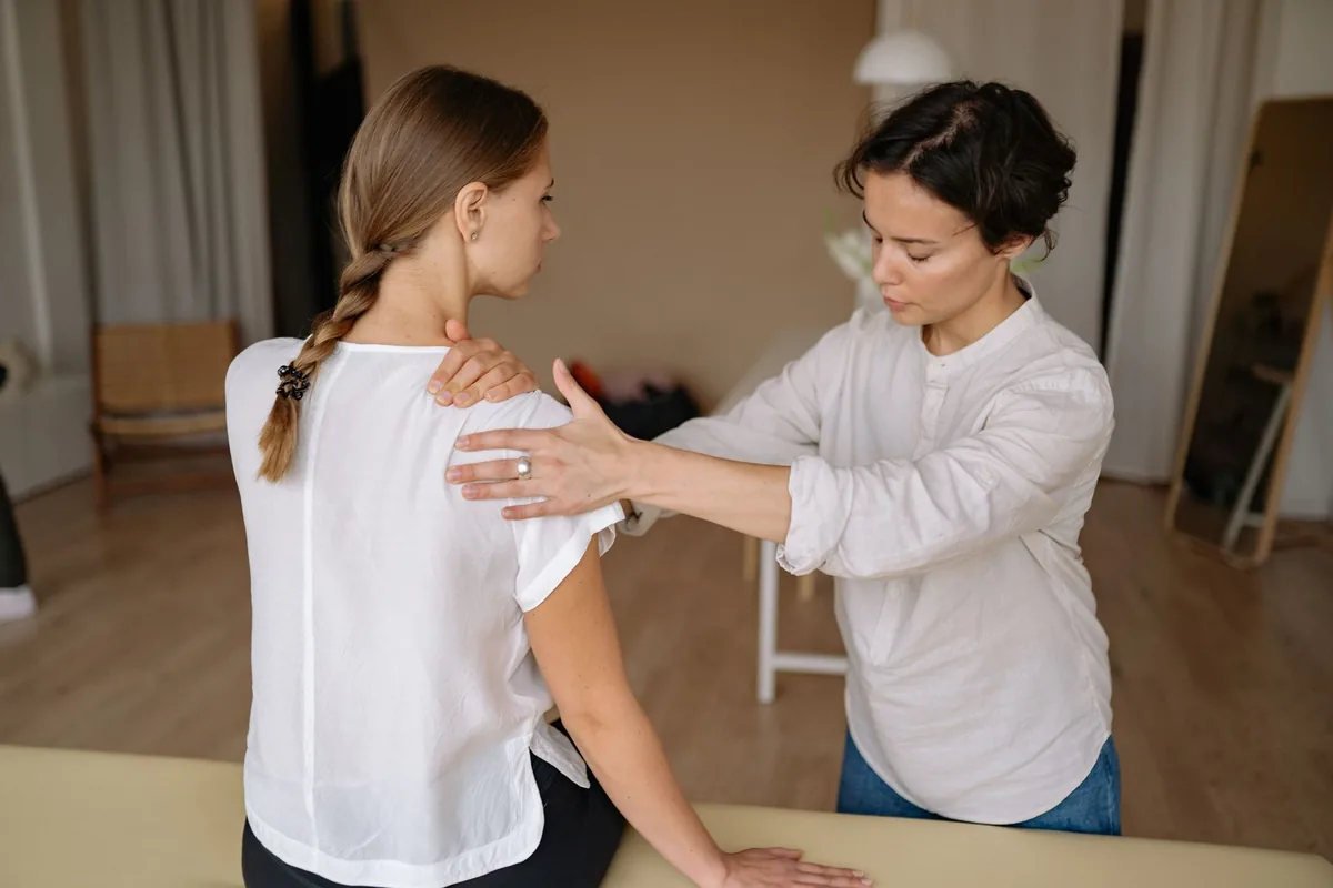 Profissional de saúde avalia o ombro de uma paciente sentada, com a mão sobre a articulação